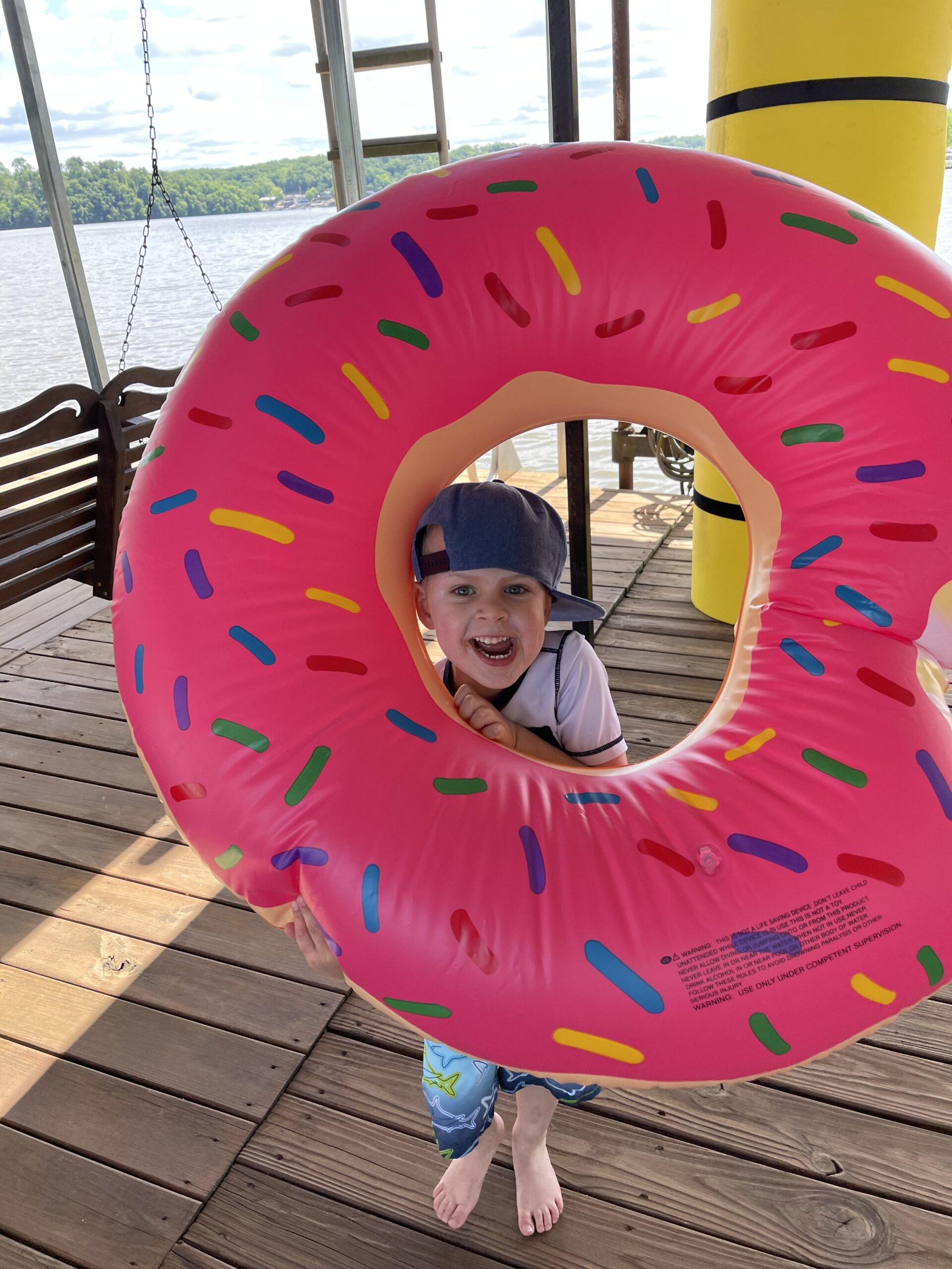 Boy on a dock smiling with his head between a donut raft