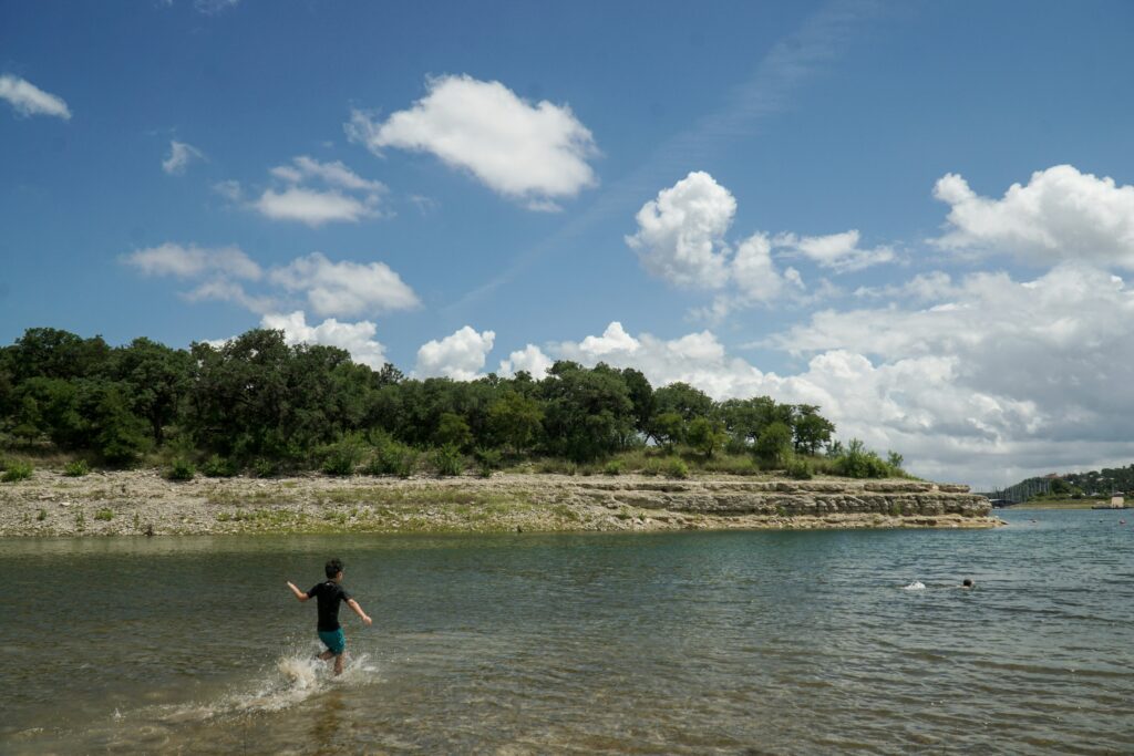 Young kid running through shallow water to go play and swim in Lake Travis