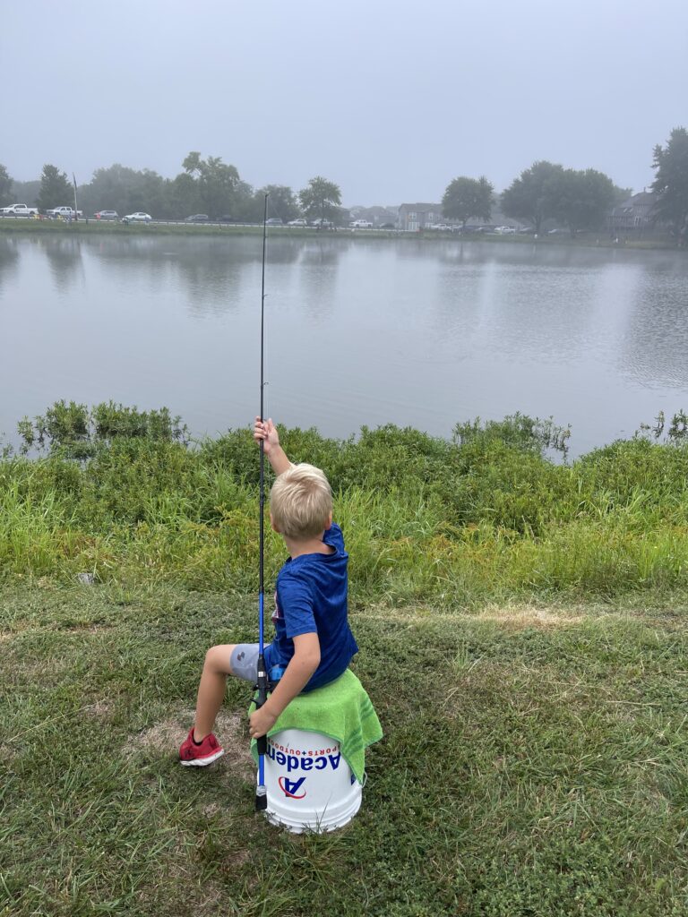 Kid sitting on a white bucket with a fishing pole next to the foggy lake