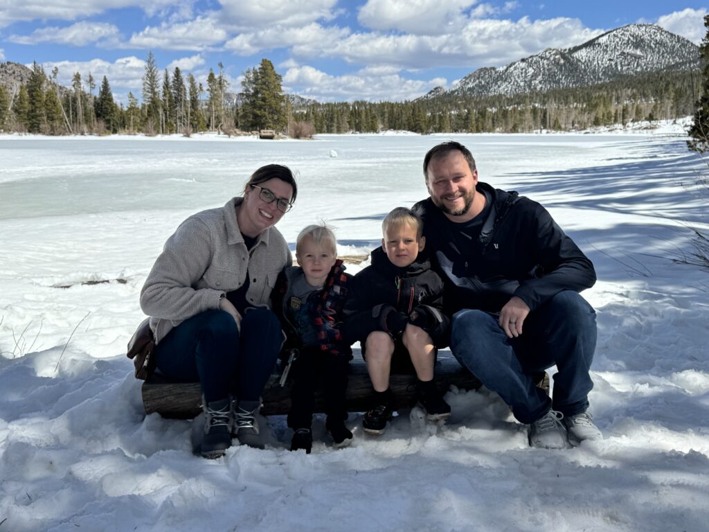 Family with two young boys sitting in the snow in front of Bear Lake Colorado