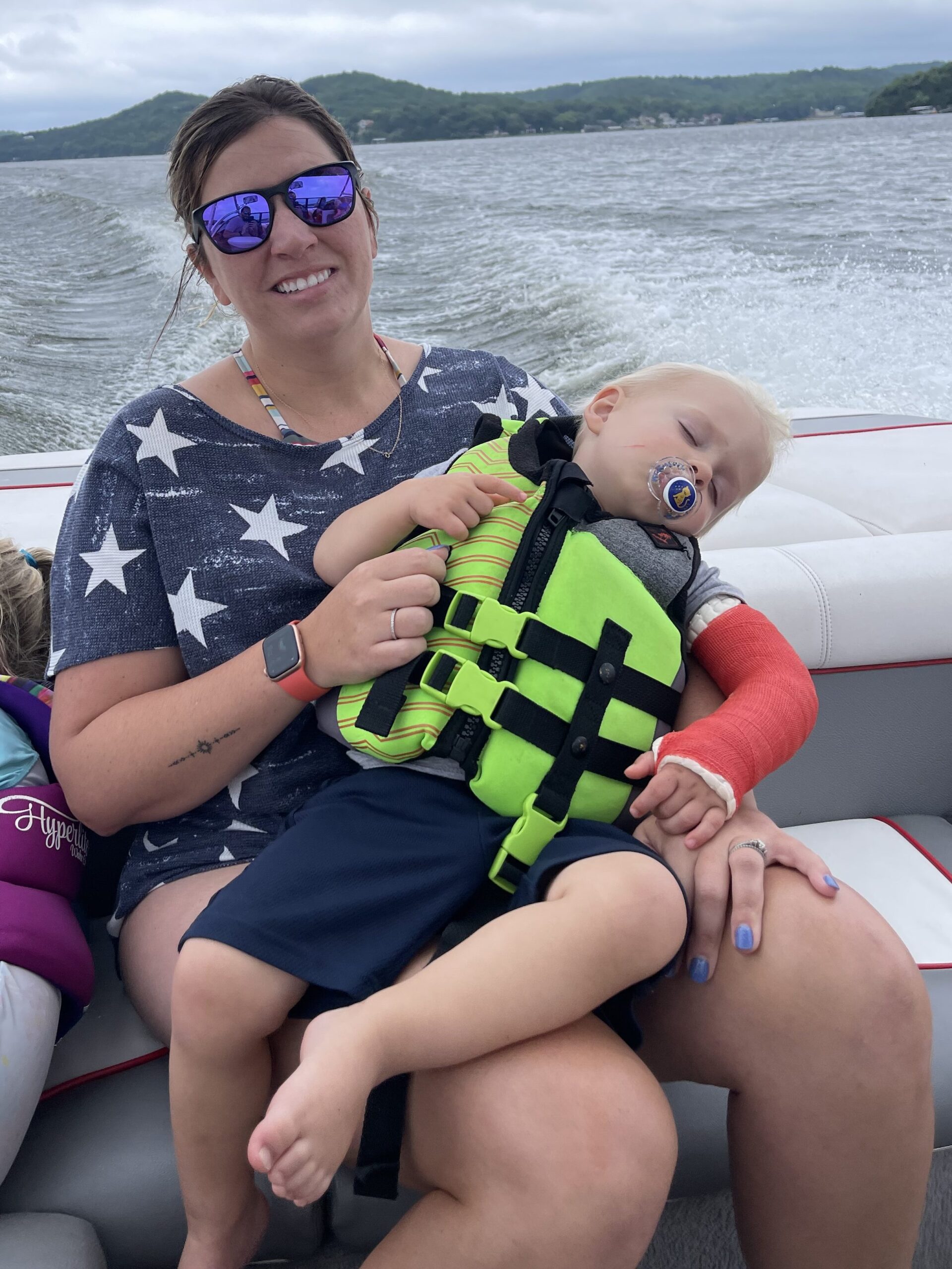 Baby sleeping in moms arms riding in the back of a boat on a lake