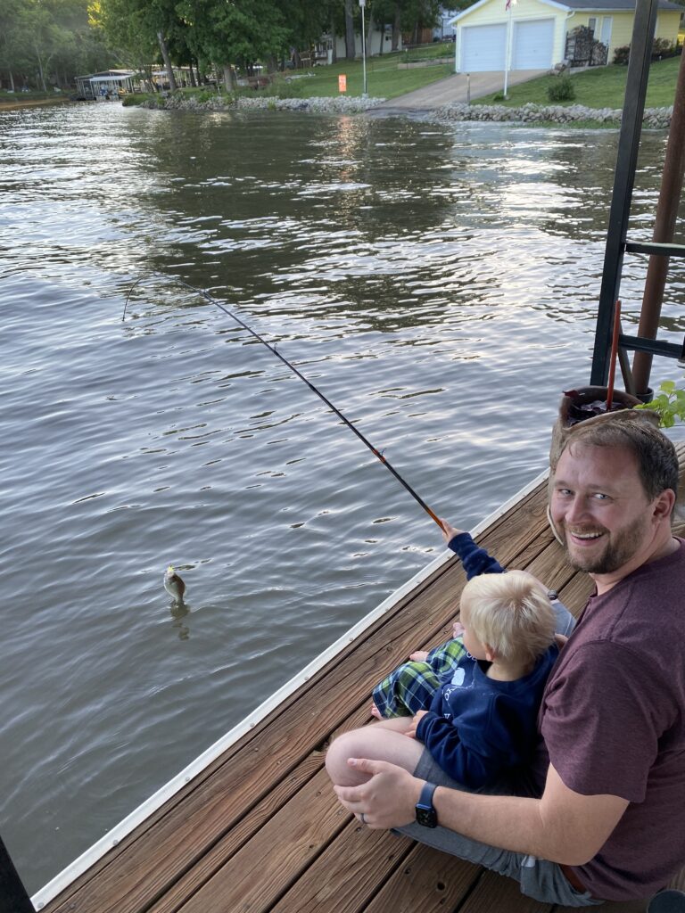 Dad and son catching a fish from the dock at the lake