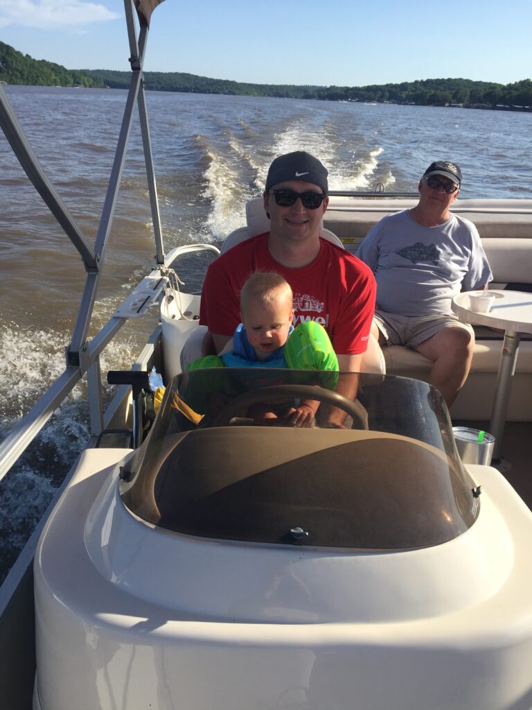 Dad and Grandpa in background with baby in lap driving a boat