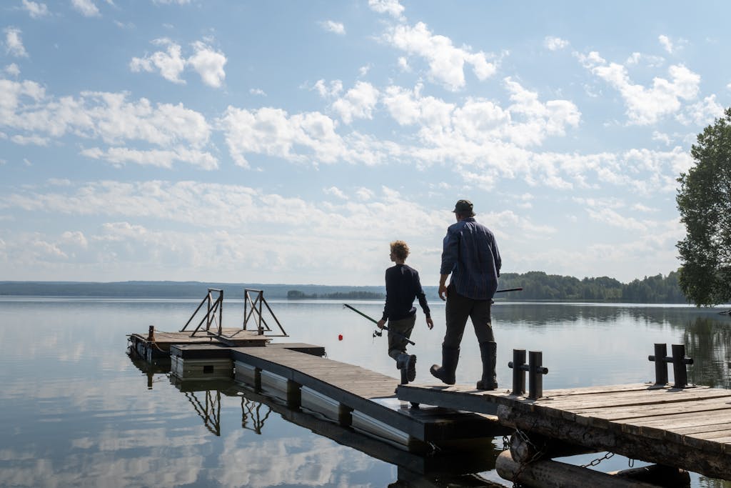 A grandfather and grandson enjoy a sunny day fishing on a peaceful lakeside pier.