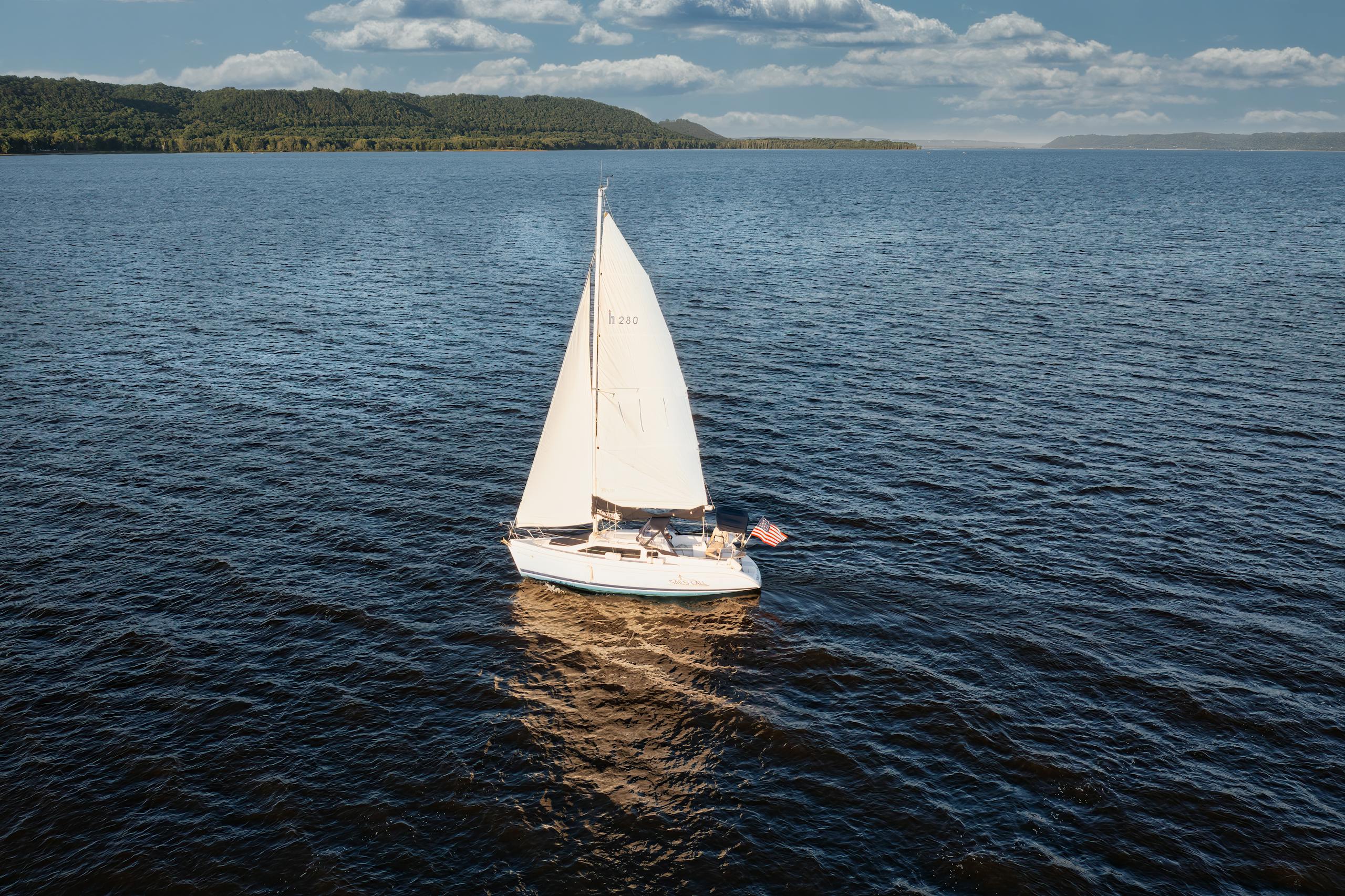 A serene aerial view of a sailboat navigating the waters of Lake City, MN, under a clear blue sky.