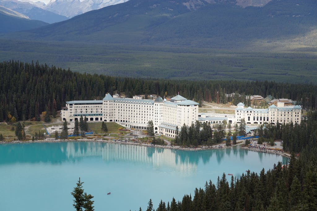 A stunning aerial view of Fairmont Chateau Lake Louise with turquoise waters and forested mountains in Canada.