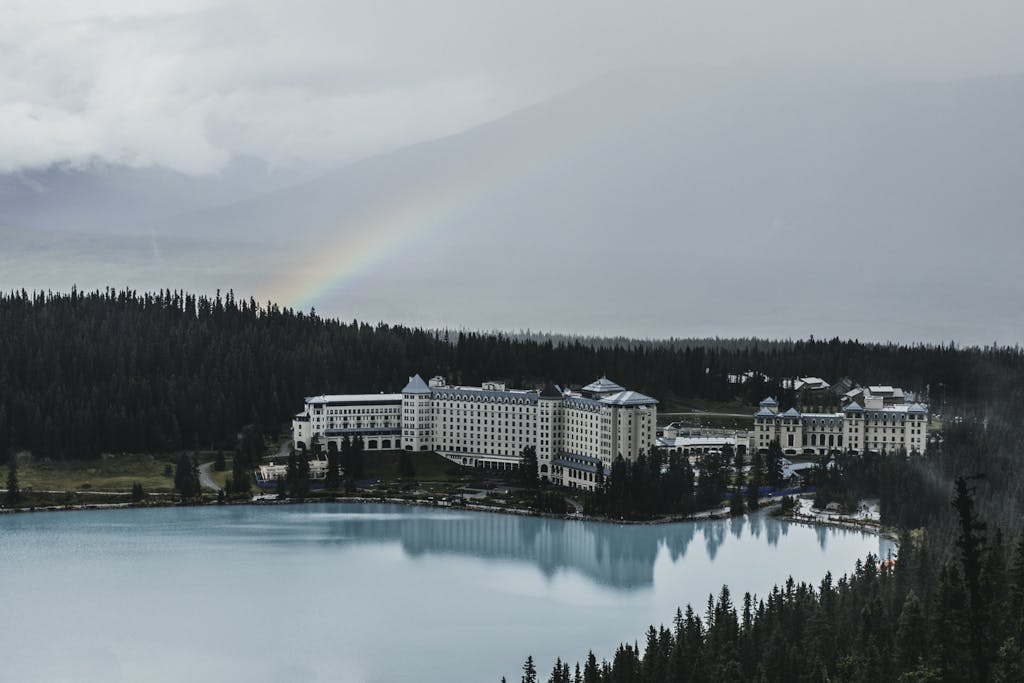 A tranquil lakeside resort surrounded by forest and a rainbow in an overcast sky.