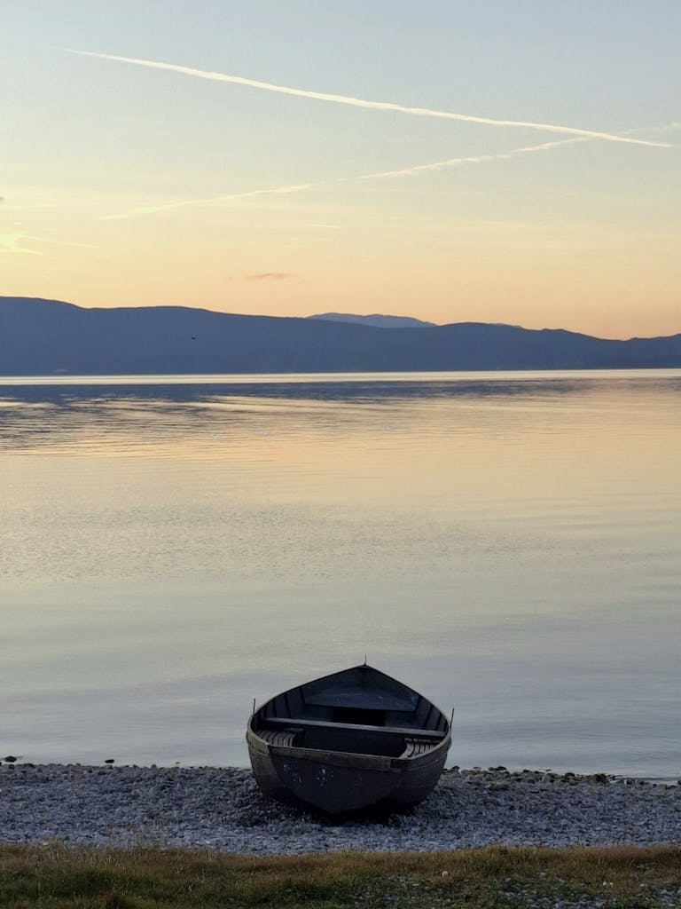 A tranquil scene of a lone boat by Lake Ohrid during a calm sunset.