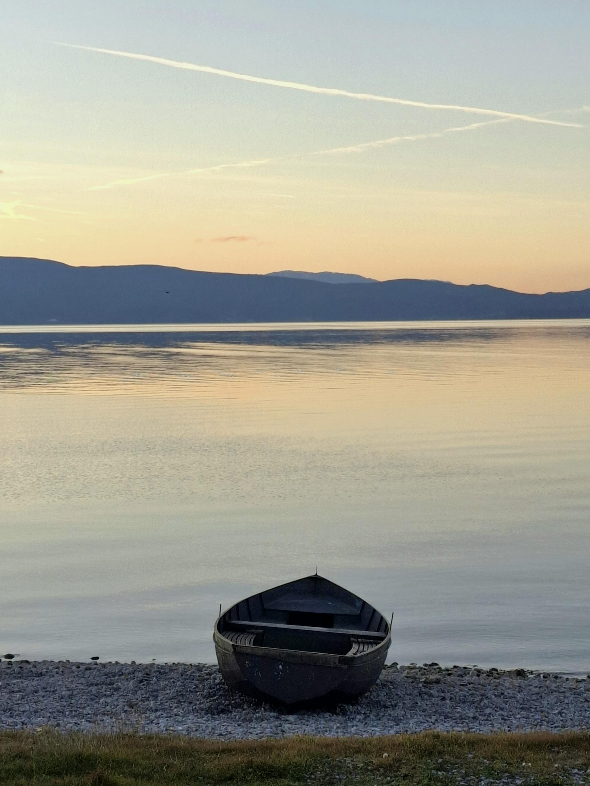 A tranquil scene of a lone boat by Lake Ohrid during a calm sunset.