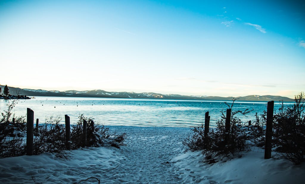 A tranquil view of a snowy beach and blue waters at Lake Tahoe during winter.