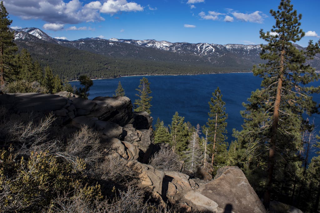 Breathtaking view of Lake Tahoe with surrounding forests and mountains, captured from a rocky cliff.