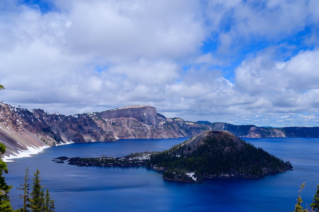 Dramatic view of Crater Lake with Wizard Island surrounded by clouds and conifer trees.