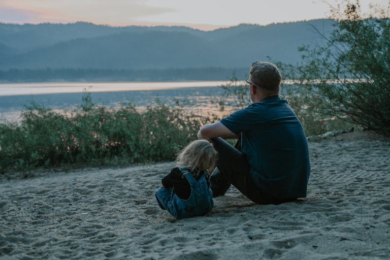 Father and child enjoy serene moments by the lakeside at dusk, surrounded by nature's tranquility.