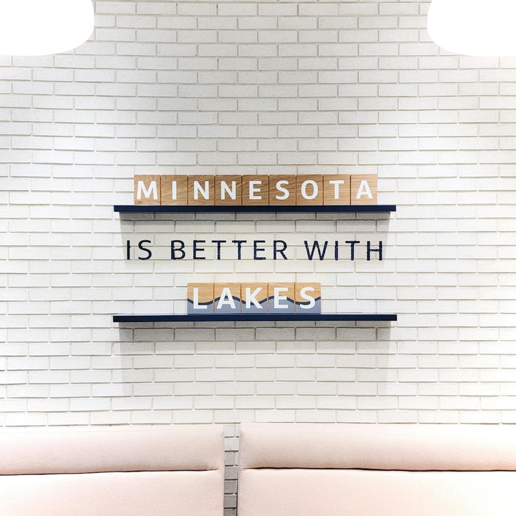 Modern wall decor highlighting Minnesota's love for lakes with letter tiles on a brick wall.