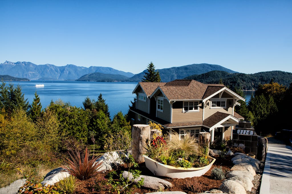 Scenic view of a charming house by the lake surrounded by mountains and lush greenery.