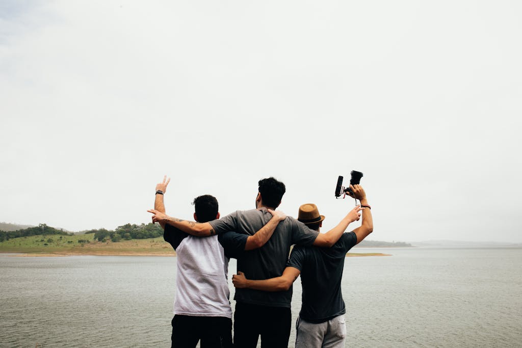 Three adult men embrace and pose by a tranquil lake, celebrating friendship and adventure.