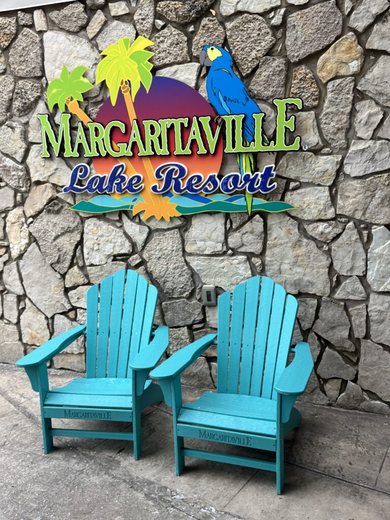 Two teal adirondeck chairs in from of the Margaritaville Lake Resort sign