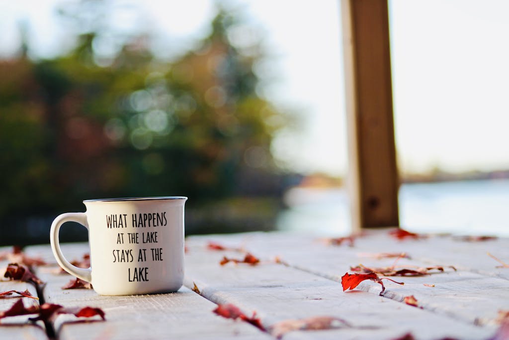 Relaxing morning by the lake with a coffee cup on a rustic table surrounded by autumn leaves.