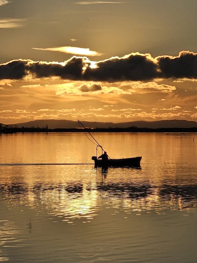 Silhouette of a person fishing in a boat during a breathtaking sunset over a tranquil lake.