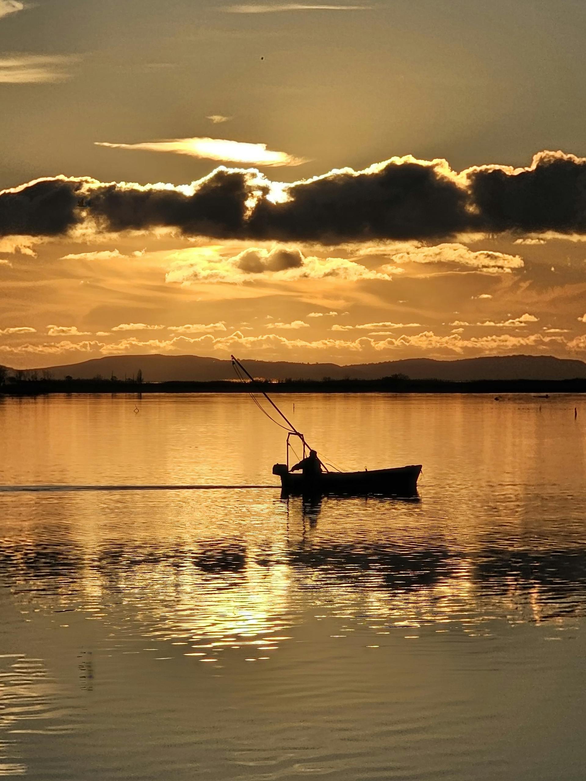 Silhouette of a person fishing in a boat during a breathtaking sunset over a tranquil lake.