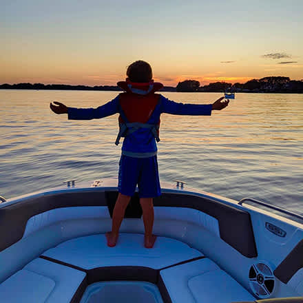 Kid at Sunset in front of a boat with arms out on Lake Norman