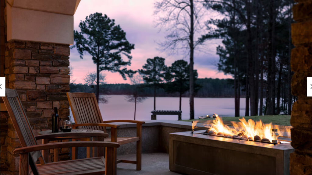 Two chairs next to a gas fire overlooking the lake at sunset