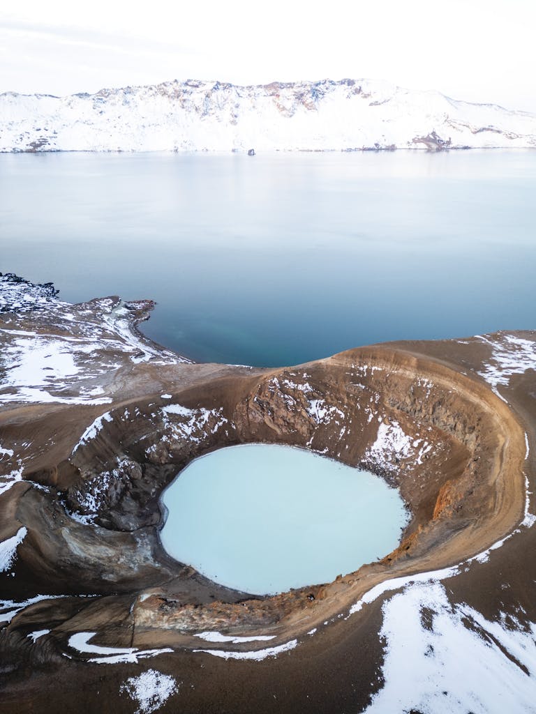 A serene aerial view capturing a crater lake amidst a snowy and rugged volcanic landscape.