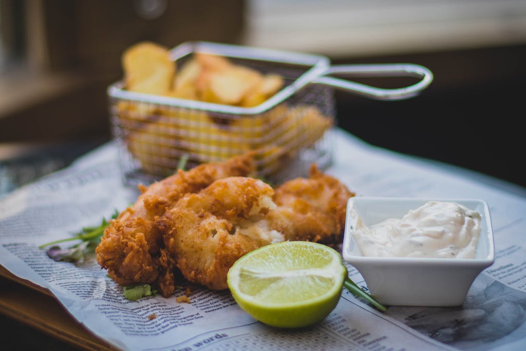 Close-up of fried fish and chips with tartar sauce and lime, perfect for food lovers.